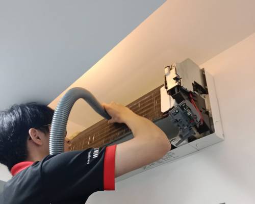 Professional Aircon Repair and Deep Cleaning Services in Singapore A technician meticulously cleaning the interior of a high-mounted air conditioning unit using a flexible vacuum hose, with the front panel open to reveal the internal components.