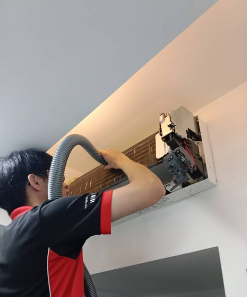 Professional Aircon Repair and Deep Cleaning Services in Singapore A technician meticulously cleaning the interior of a high-mounted air conditioning unit using a flexible vacuum hose, with the front panel open to reveal the internal components.