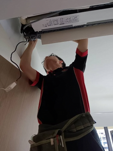 Precision Installation and Repair: Aircon Servicing Singapore A skilled technician in a red and black shirt, equipped with a tool belt, is meticulously repairing or installing a wall-mounted air conditioning unit, with cables hanging from the open compartment.